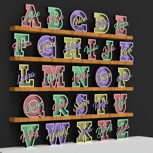 May include: A display of colorful, illuminated wooden letters, each with a name, arranged on wooden shelves. The letters are in various pastel colors, including pink, green, and yellow. The names are written in a cursive font.