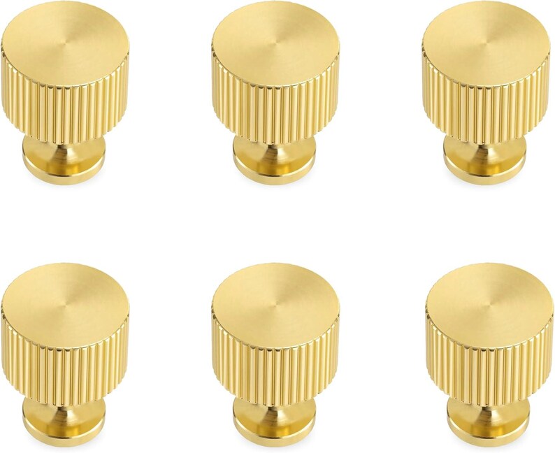 Pode incluir: Seis puxadores dourados para arm&aacute;rios. Cada puxador tem formato cil&iacute;ndrico com textura canelada nas laterais e um topo liso e circular. Os puxadores s&atilde;o montados em uma pequena base arredondada.