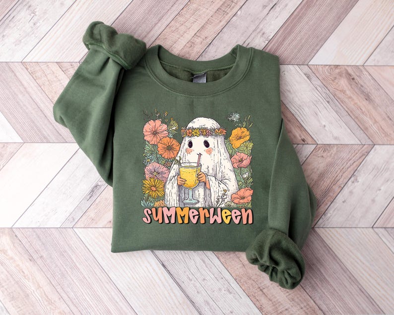 May include: Green sweatshirt with a ghost graphic wearing a floral crown and holding a drink. The design includes colourful flowers and the word "SUMMERWEEN". The sweatshirt has cuffed sleeves.