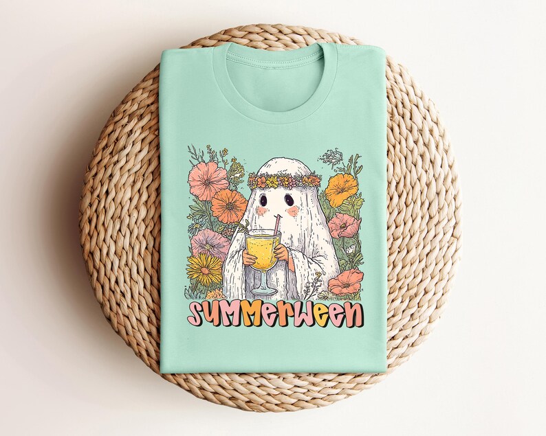 May include: Mint green t-shirt with a cartoon ghost wearing a flower crown and holding a drink. The ghost is surrounded by colourful flowers. The text "SUMMERWEEN" is printed in a retro font.