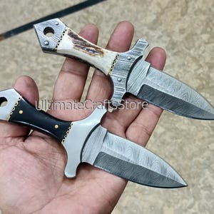 May include: Two small, decorative knives with patterned blades and ornate handles. One knife has a black handle with gold accents, while the other features a handle made of bone. The blades have a unique, textured pattern.