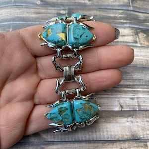 May include: Vintage bracelet with turquoise-coloured, abstract-shaped stones with gold flecks, set in silver-tone metal. The bracelet has a unique design with articulated links and a secure clasp. A striking piece of jewellery.