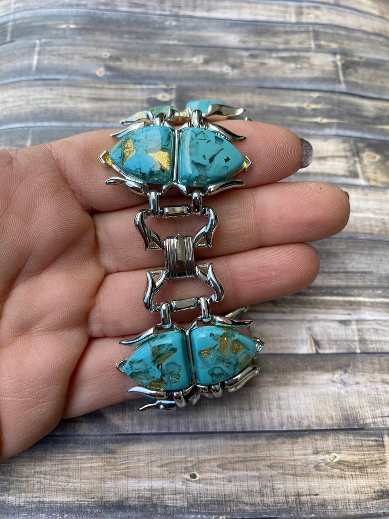 May include: Vintage bracelet with turquoise-coloured, abstract-shaped stones with gold flecks, set in silver-tone metal. The bracelet has a unique design with articulated links and a secure clasp. A striking piece of jewellery.