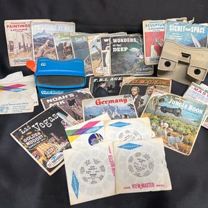 May include: A collection of vintage View-Master reels and viewers. The image includes various reel packets with titles like "Las Vegas," "Jungle Book," and "Noah's Ark." A blue 3D viewer and several small booklets are also present.