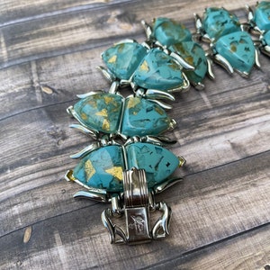 May include: Vintage turquoise and gold-flecked bracelet with silver-tone metal accents. The bracelet features a series of stylized, geometric shapes. The clasp is marked with a maker's mark. The bracelet is a statement piece.