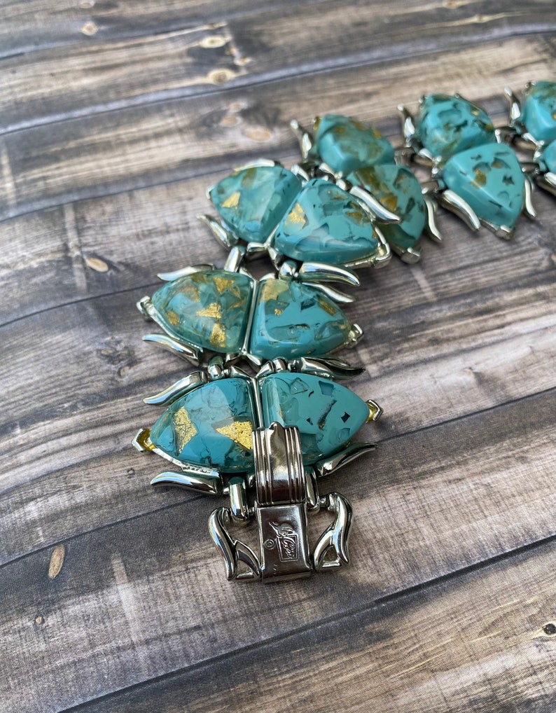 May include: Vintage turquoise and gold-flecked bracelet with silver-tone metal accents. The bracelet features a series of stylized, geometric shapes. The clasp is marked with a maker's mark. The bracelet is a statement piece.