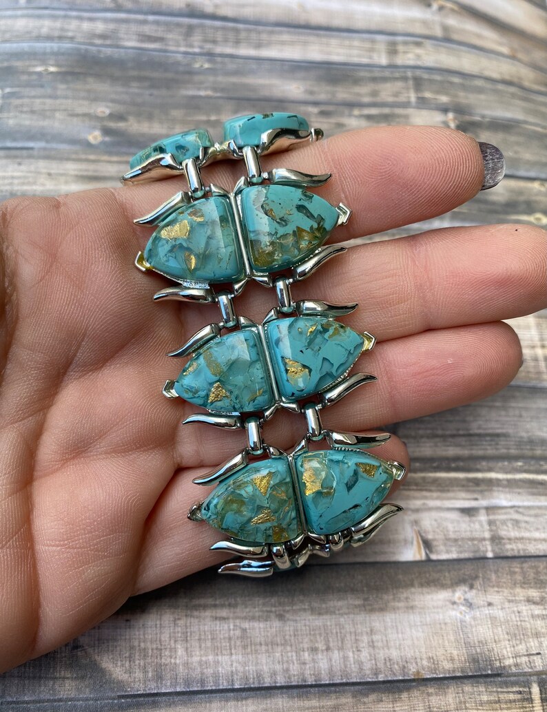 May include: A vintage bracelet with six turquoise beetle-shaped links, each with gold flecks, joined by silver-toned metal. The bracelet is held in a hand, highlighting its intricate design and colour palette.
