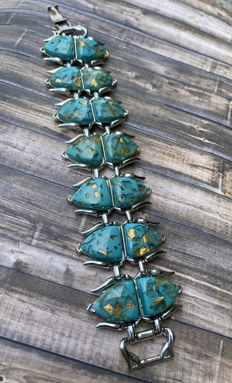 May include: A vintage bracelet with turquoise beetle-shaped links, adorned with gold flecks, linked by silver-toned metal. The bracelet is displayed on a wooden surface, highlighting its unique design and colour palette.