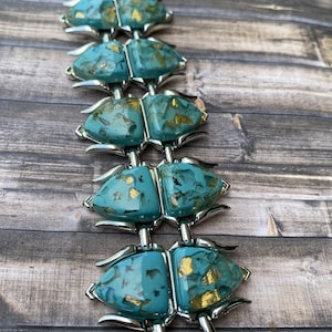 May include: A vintage bracelet with turquoise-coloured, abstract links with gold flecks, joined by silver-toned metal. The bracelet is displayed on a wooden surface, highlighting its unique design and colour palette.