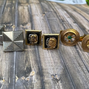 May include: Set of six cufflinks, two silver with geometric designs, two black with gold-toned profile images of men wearing helmets, and two gold with green gemstones in the center.