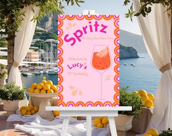 May include: A pink sign with the word "Spritz" in large, bright pink letters. The sign also says "Me Baby One More Time" and "Welcome to Lucy's 21st birthday". A graphic of a cocktail glass is also on the sign.