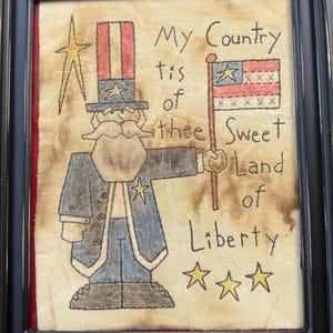 May include: Framed folk art featuring a patriotic Uncle Sam figure holding a flag. The artwork includes the text "My Country 'tis of thee Sweet Land of Liberty" and star accents. The frame is black.
