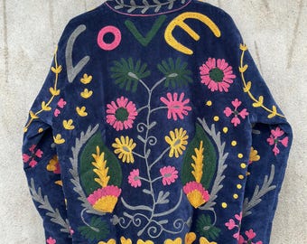 Könnte beinhalten: Eine dunkelblaue Jacke mit farbenfroher Stickerei. Auf der Rückseite ist das Wort LOVE in großen Buchstaben über einem Blumenmuster mit rosa, gelben und grünen Blüten, Blättern und kleinen gelben Herzen am unteren Saum zu sehen.