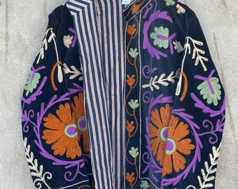 May include: A black jacket featuring vibrant floral embroidery in orange, purple, and light green. The jacket has a stand-up collar and an open front that reveals a contrasting interior lining with thin vertical navy blue and white stripes.