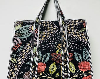 Könnte beinhalten: Schwarze, gesteppte Tragetasche mit einem Blumenmuster in Rot-, Grün- und Gelbtönen. Die Tasche hat gestreifte Griffe und Verzierungen. Die Tasche hängt an einer Wand.