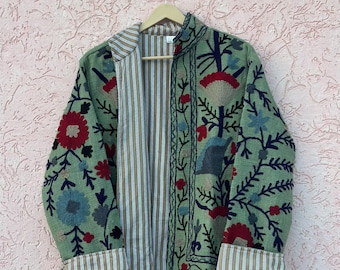 May include: A long-sleeved jacket featuring a green base with embroidered floral patterns in red, blue, and dark navy. The interior and cuffs are lined with a tan and white vertical striped fabric. The jacket has a high collar and open front.