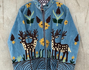 May include: A light blue zip-up jacket featuring dark brown deer silhouettes with white spots, yellow flower embroidery, and dark brown curved line patterns along the hem. The jacket has a stand-up collar and long sleeves with a striped inner lining.