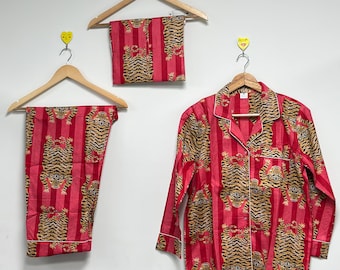 Könnte beinhalten: Ein rotes Pyjama-Set mit Tigerstreifenmuster, bestehend aus einem langärmeligen Hemd mit Knöpfen, einer Hose und einem passenden Schal. Das Set wird auf Holzbügeln vor einer weißen Wand präsentiert.