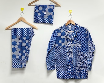 Könnte beinhalten: Blau-weißes Pyjama-Set mit verschiedenen Mustern, darunter Kreise und geometrische Formen. Das Set besteht aus einem langärmeligen Hemd mit Knöpfen, einer Hose und einem gefalteten Artikel, alles auf Holzbügeln an einer weißen Wand.