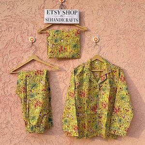May include: A yellow pajama set featuring a vibrant floral and palm leaf print in red, green, and white. The set includes a long-sleeved button-down shirt with a collar and matching pants, displayed alongside a folded fabric piece and a sign reading ETSY SHOP SEHANDICRAFTS.