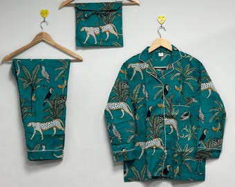 Könnte beinhalten: Türkisfarbenes Pyjama-Set mit Dschungel-Print mit Leoparden, Tukanen und Palmen. Das Set beinhaltet ein Hemd mit Knöpfen, eine Hose und einen passenden Reisebeutel, alles mit weißem Paspel verziert. Die Pyjamas hängen an Holzbügeln.