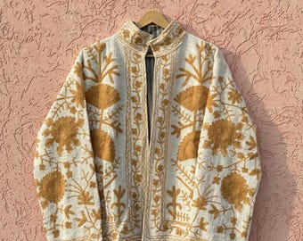 May include: A long-sleeved jacket in off-white fabric featuring intricate mustard yellow floral embroidery throughout the front and sleeves. The garment has a high collar, an open front design, and a visible striped lining on the inner collar.