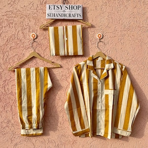 May include: A pajama set featuring a long-sleeved button-down shirt and matching pants with a mustard yellow and off-white vertical stripe pattern. A folded fabric piece and a sign reading ETSY SHOP SEHANDICRAFTS are displayed above.
