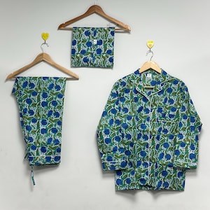 Könnte beinhalten: Ein Set aus blau-grünen Pyjamas mit floralem Muster, bestehend aus einem langärmeligen Hemd mit Knöpfen, einer Hose und Shorts, die alle an Holzbügeln hängen. Die Pyjamas haben weiße Paspeln.