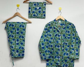 Könnte beinhalten: Ein Set aus blau-grünen Pyjamas mit floralem Muster, bestehend aus einem langärmeligen Hemd mit Knöpfen, einer Hose und Shorts, die alle an Holzbügeln hängen. Die Pyjamas haben weiße Paspeln.