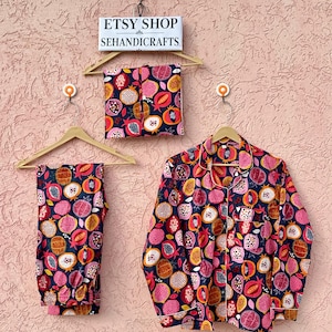 Puede incluir: Un conjunto de pijama compuesto por una camisa de manga larga con botones y pantalones a juego, en tela azul oscuro con un patrón repetitivo de granadas rosas, rojas y naranjas. Un letrero arriba dice ETSY SHOP SEHANDICRAFTS.