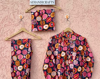 May include: A pyjama set consisting of a long-sleeved button-down shirt and matching trousers, featuring a dark blue fabric with a repeating pattern of pink, red, and orange pomegranates. A sign above reads ETSY SHOP SEHANDICRAFTS.