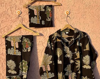 Könnte beinhalten: Ein schwarzer Schlafanzug bestehend aus einem langärmeligen Hemd mit Knopfleiste und einer passenden Hose mit einem wiederkehrenden botanischen Druck von Bäumen und Blättern in Grün-, Weiß- und Orangetönen. Ein Schild darüber zeigt ETSY SHOP SEHANDICRAFTS.