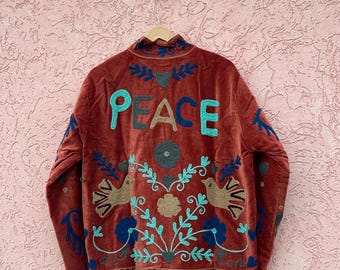 Könnte beinhalten: Eine rostfarbene Samtjacke mit dem Wort PEACE, das in großen Buchstaben auf den Rücken gestickt ist. Das Design zeigt florale Muster, Blätter und Vogelmotive in Türkis, Dunkelblau und Beige, mit einem Stehkragen und langen Ärmeln.