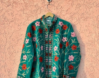 Könnte beinhalten: Eine langärmelige, blaugrüne Jacke mit einem gestickten Blumenmuster in Rot- und Rosatönen. Die Jacke verfügt über einen Stehkragen, eine durchgehende Vorderseite und gerade Ärmelabschlüsse, wobei sich die Stickerei über die Vorderseite erstreckt.
