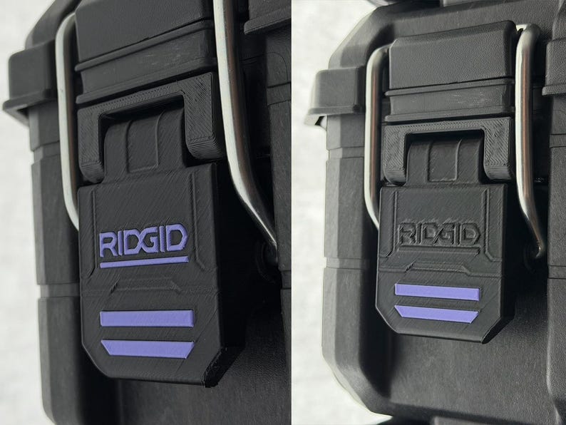 Puede incluir: Primer plano de un cierre de malet&iacute;n de herramientas negro con el nombre de la marca "RIDGID" en letras blancas y dos rayas horizontales moradas. El cierre est&aacute; hecho de un material duradero y texturizado y tiene una bisagra de metal plateado.