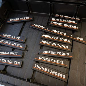 Puede incluir: Un organizador de caja de herramientas negro con etiquetas para la organizaci&oacute;n de herramientas. Las etiquetas incluyen "Spare Parts", "Sockets", "Screwdrivers" e "Impact Drivers". Otras etiquetas dicen "Move a Lot", "Random Shit" y "Problem Solver".