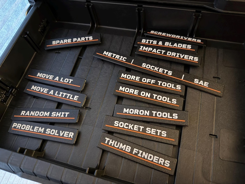 Puede incluir: Un organizador de caja de herramientas negro con etiquetas para la organizaci&oacute;n de herramientas. Las etiquetas incluyen "Spare Parts", "Sockets", "Screwdrivers" e "Impact Drivers". Otras etiquetas dicen "Move a Lot", "Random Shit" y "Problem Solver".