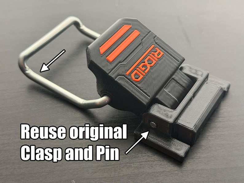 Puede incluir: Pieza de repuesto impresa en 3D en negro y naranja con la palabra "RIDGID" en naranja. Se adjunta un cierre de metal plateado. El texto "Reuse original Clasp and Pin" est&aacute; en la imagen. Esta es una pieza de repuesto para herramientas.
