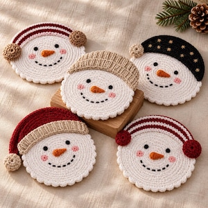 May include: Five circular crochet coasters shaped like snowman faces. Each features a white face with black eyes, a stitched orange carrot nose, pink cheeks, and a black dotted smile. They wear various hats and earmuffs in red, black, and tan.