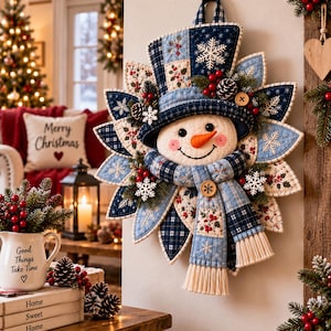 Peut inclure: Une décoration murale en tissu matelassé représentant un bonhomme de neige avec un chapeau haut-de-forme bleu et blanc, une écharpe assortie à franges et un nez orange. L'ensemble est orné de flocons de neige blancs, de baies rouges et de pommes de pin.
