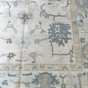 K&ouml;nnte beinhalten: Hellgrauer Teppich mit detailliertem Blumenmuster in Blau-, Beige- und Gr&uuml;nt&ouml;nen. Der Teppich hat einen verzierten Rand und einen Used-Look im Vintage-Stil, geeignet f&uuml;r Wohn- oder Schlafzimmer.