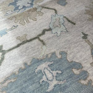 K&ouml;nnte beinhalten: Nahaufnahme eines beigefarbenen Teppichs mit einem Blumenmuster in Blau- und Gr&uuml;nt&ouml;nen. Der Teppich hat eine strukturierte Oberfl&auml;che und ein traditionelles Design, geeignet f&uuml;r die Inneneinrichtung.