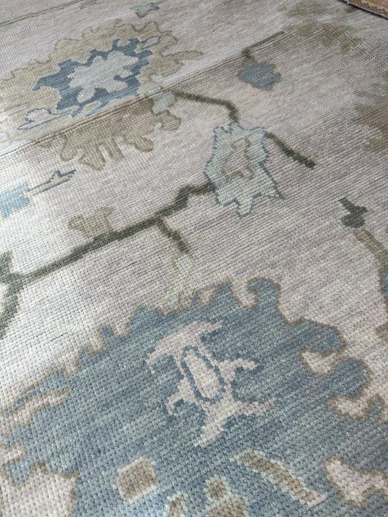 K&ouml;nnte beinhalten: Nahaufnahme eines beigefarbenen Teppichs mit einem Blumenmuster in Blau- und Gr&uuml;nt&ouml;nen. Der Teppich hat eine strukturierte Oberfl&auml;che und ein traditionelles Design, geeignet f&uuml;r die Inneneinrichtung.