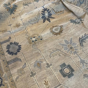 May include: A beige area rug with a detailed floral pattern in shades of blue, gray, and brown. The rug features an intricate design with stylized flowers and geometric shapes, creating a vintage or traditional aesthetic.