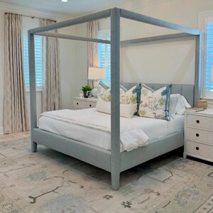 K&ouml;nnte beinhalten: Ein hellblaues Himmelbett mit wei&szlig;er Bettw&auml;sche und dekorativen Kissen. Das Schlafzimmer verf&uuml;gt &uuml;ber einen gemusterten Teppich, wei&szlig;e Nachttische und transparente Vorh&auml;nge. Eine gro&szlig;e Deckenleuchte h&auml;ngt von der Decke.