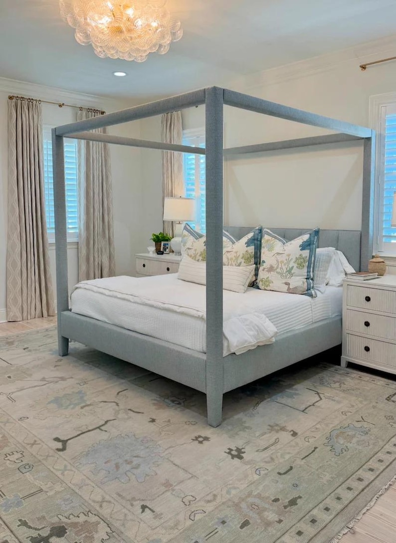 K&ouml;nnte beinhalten: Ein hellblaues Himmelbett mit wei&szlig;er Bettw&auml;sche und dekorativen Kissen. Das Schlafzimmer verf&uuml;gt &uuml;ber einen gemusterten Teppich, wei&szlig;e Nachttische und transparente Vorh&auml;nge. Eine gro&szlig;e Deckenleuchte h&auml;ngt von der Decke.