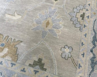 Könnte beinhalten: Nahaufnahme eines hellfarbenen Teppichs mit detailliertem Blumenmuster. Der Teppich weist eine Kombination aus Beige, Hellblau und Olivgrün auf. Das Design umfasst stilisierte Blumen und geometrische Formen, die eine traditionelle Ästhetik schaffen.