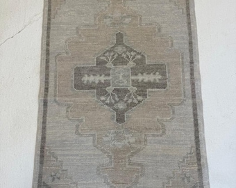 Könnte beinhalten: Rechteckiger Teppich mit einem zentralen geometrischen Design in Grau-, Beige- und Brauntönen. Der Teppich hat einen Rand und ein zentrales Medaillonmuster. Der Teppich ist wahrscheinlich aus gewebtem Material und eignet sich für die Inneneinrichtung.