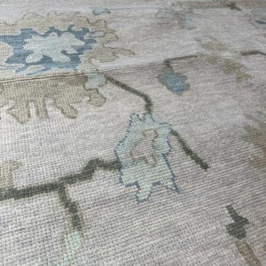 K&ouml;nnte beinhalten: Nahaufnahme eines beigefarbenen Teppichs mit einem Blumenmuster in Blau- und Gr&uuml;nt&ouml;nen. Der Teppich hat eine strukturierte Oberfl&auml;che und ein traditionelles Design, geeignet f&uuml;r die Inneneinrichtung.