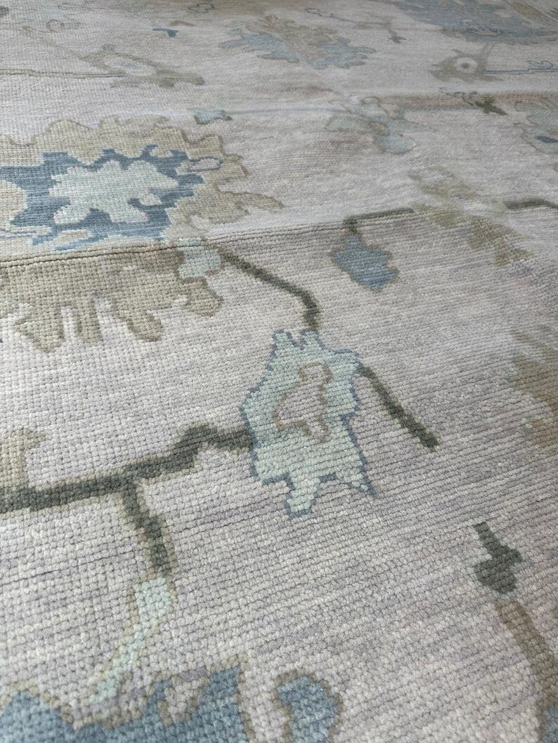 K&ouml;nnte beinhalten: Nahaufnahme eines beigefarbenen Teppichs mit einem Blumenmuster in Blau- und Gr&uuml;nt&ouml;nen. Der Teppich hat eine strukturierte Oberfl&auml;che und ein traditionelles Design, geeignet f&uuml;r die Inneneinrichtung.